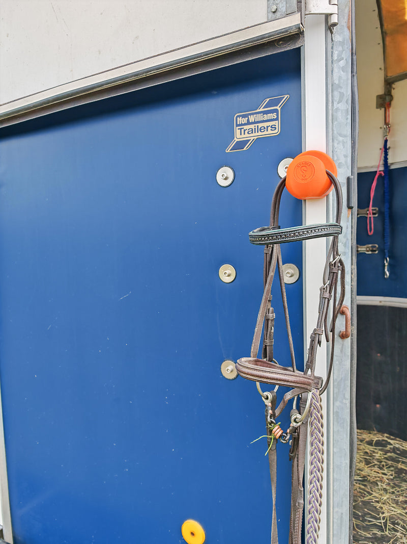 StablePin Core orange magnetic hook mounted on an Ifor Williams trailer door holding a bridle