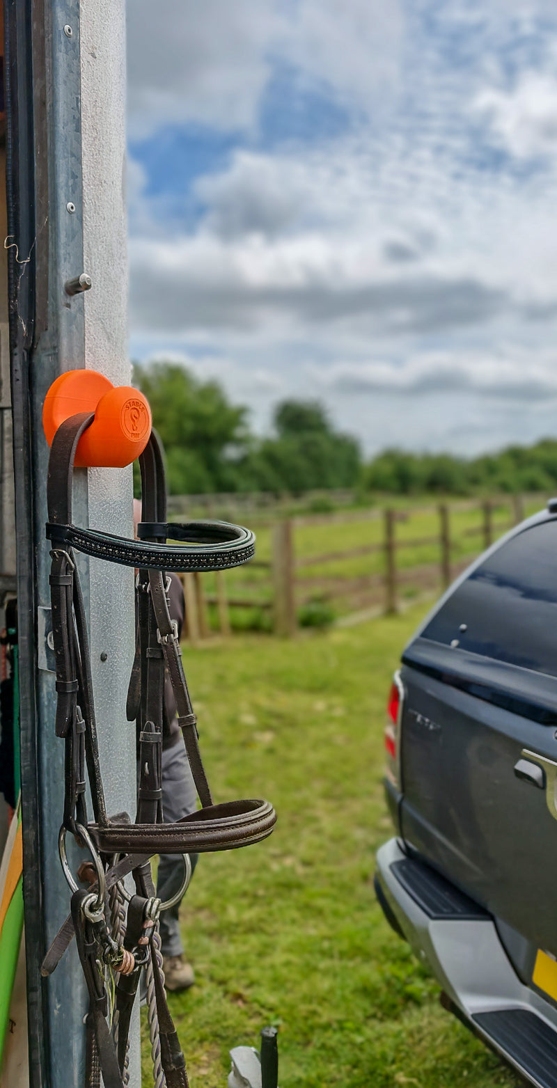 StablePin Core orange magnetic hook mounted on a trailer post holding a bridle